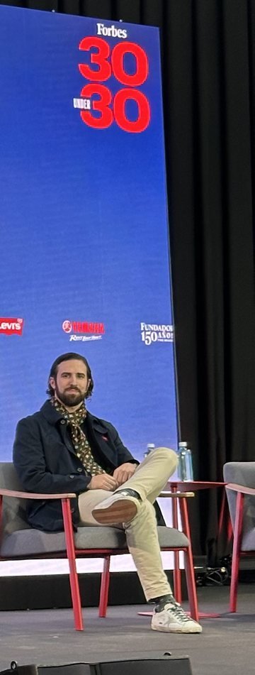 Alfonso Medela seated on stage at the Forbes 30 Under 30 Summit 2024, under the 30 Under 30 logo